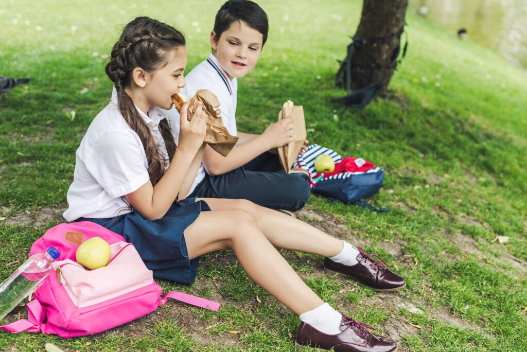 schoolchildren sitting on green grass and taking lunch